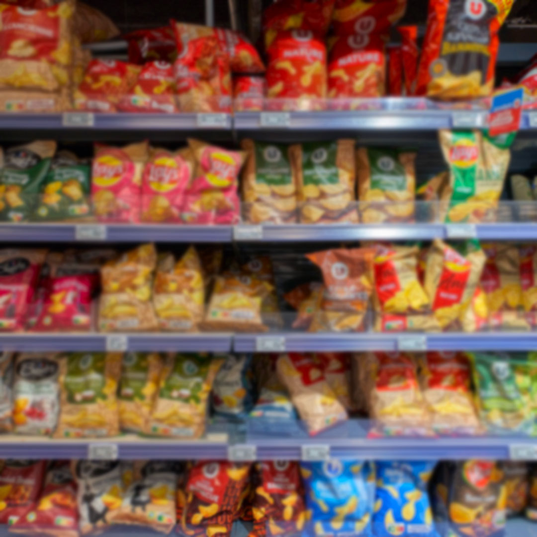 Brightly colored bags and packages of chips or other snacks on retail shelves in a grocery store setting